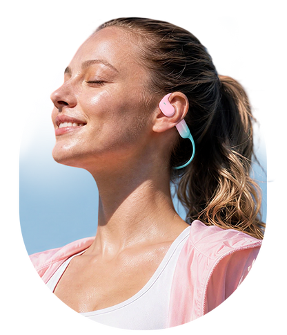 Woman walking outdoors while wearing AirWave Pro2 open-ear sports headphones in Coral Pink